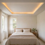 Small bedroom with white tray ceiling and warm cove lighting above a bed