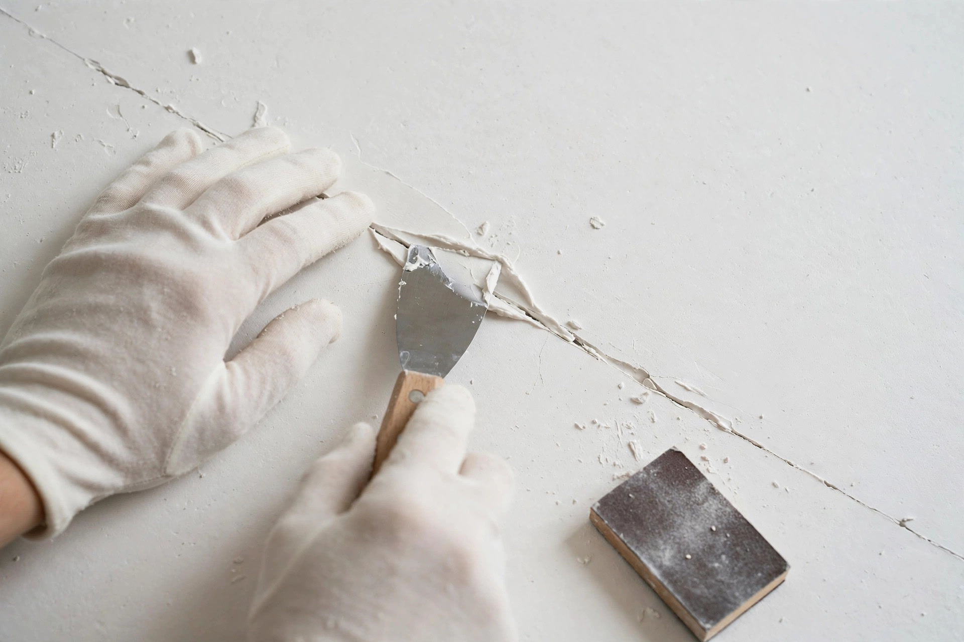 Close-up of a hairline crack in POP plaster being filled and sanded