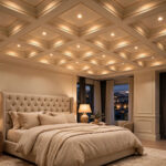 Cream coffered false ceiling with thin gold trim and warm recessed lights above a tufted bed