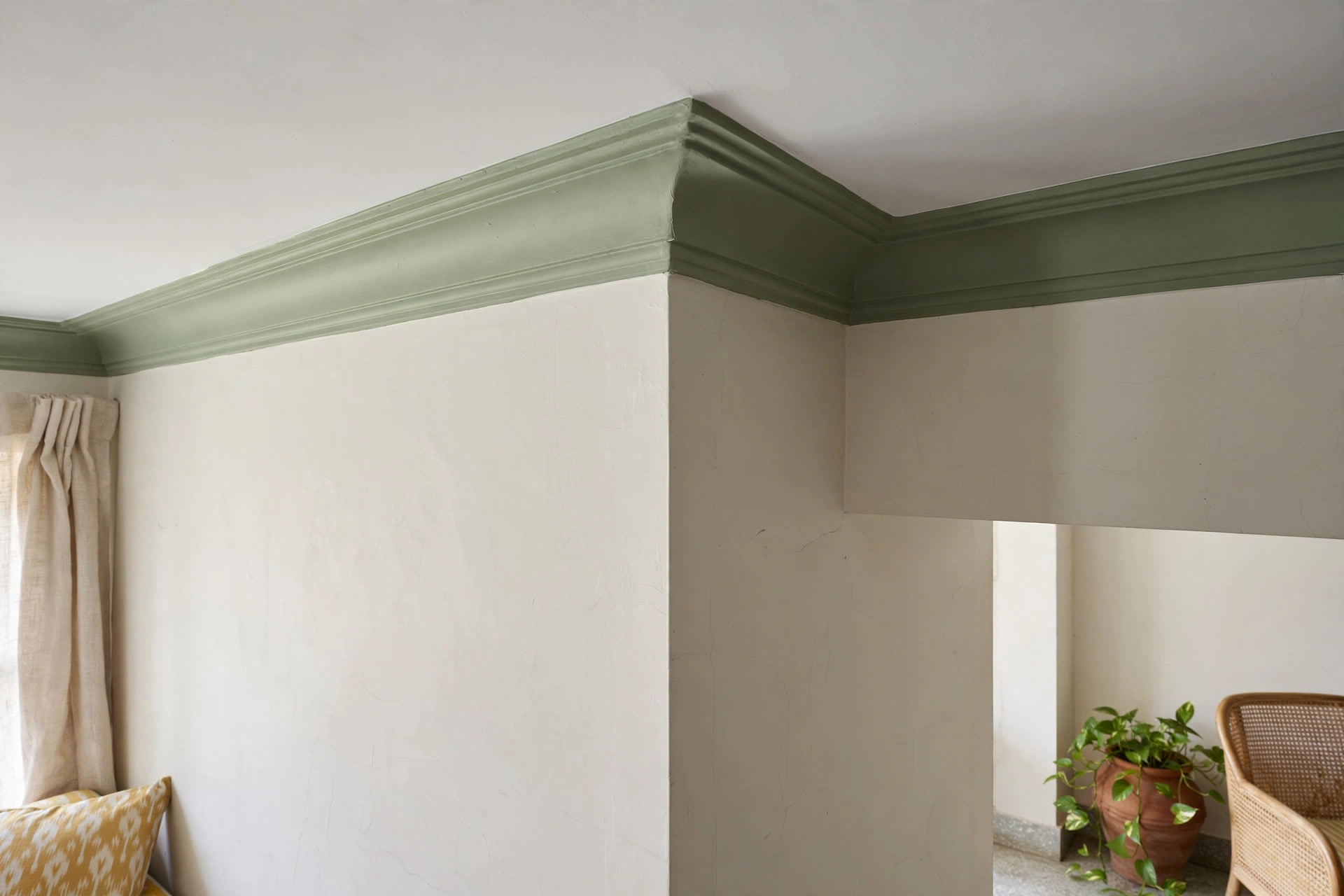 Corner detail of a cornice moulding painted sage green along a plain white ceiling edge