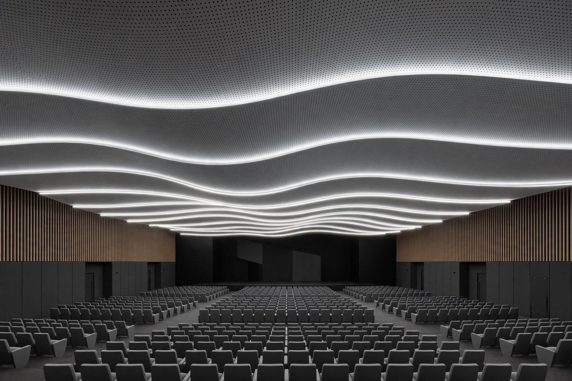Auditorium with grey micro-perforated acoustic metal ceiling panels and concealed linear lighting