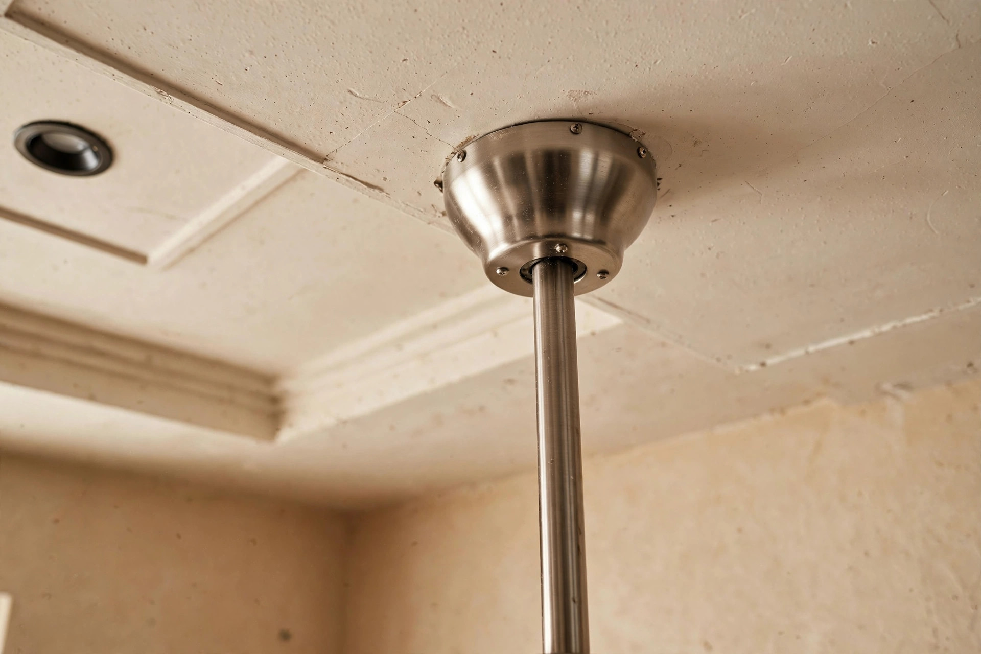 Close-up of a ceiling fan downrod mount meeting the ceiling with metal rod and canopy