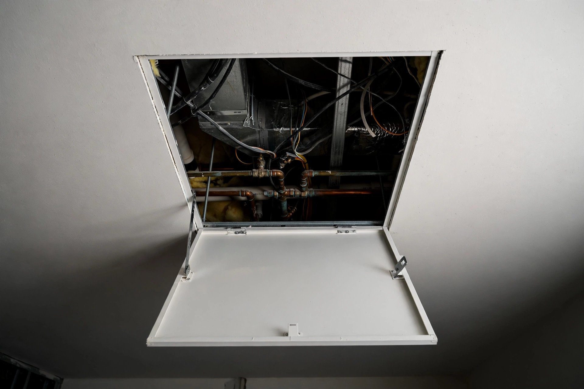 Open access panel in a gypsum false ceiling revealing wiring and pipes in the space above