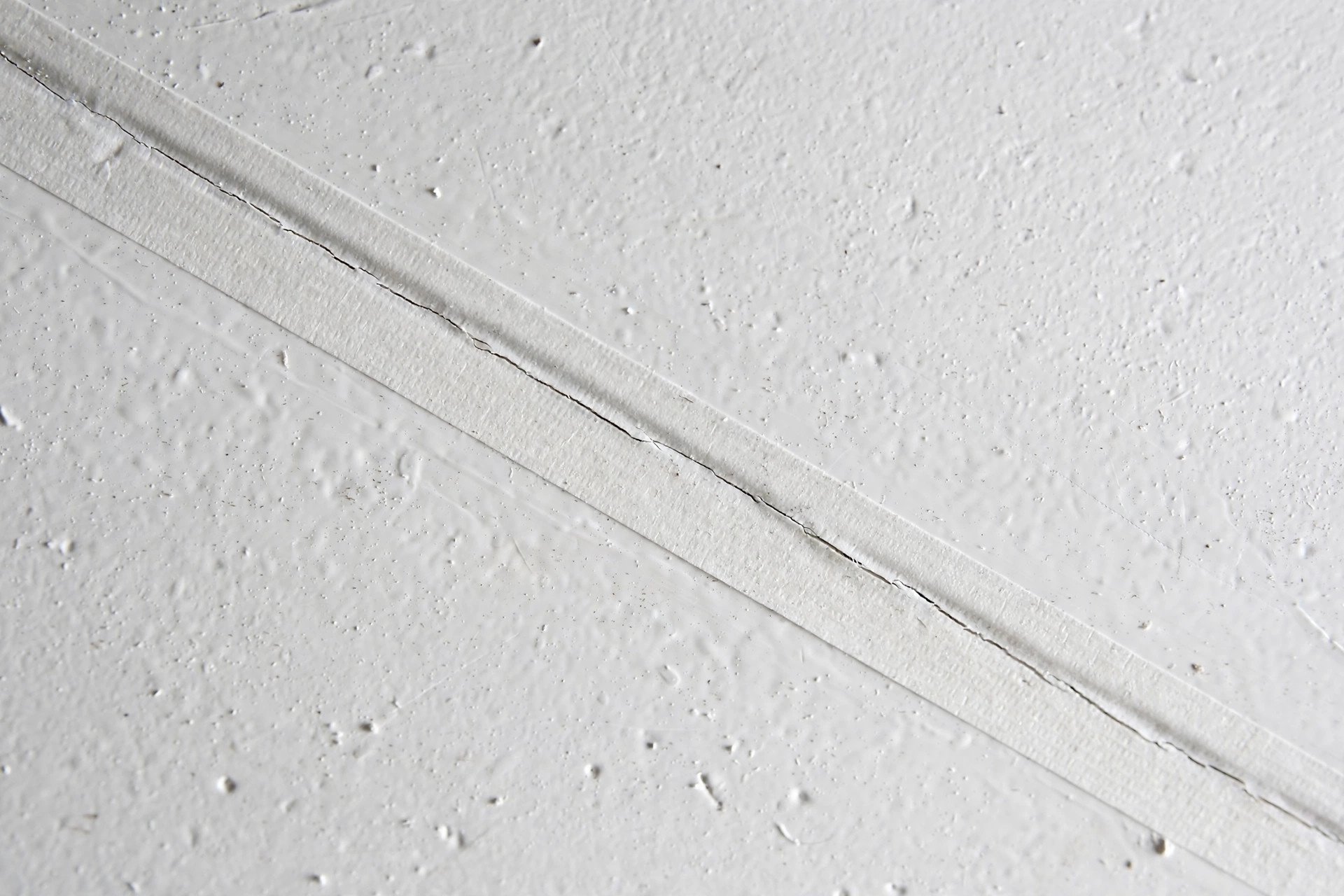 Close-up of a fine hairline crack along a joint in a painted false ceiling