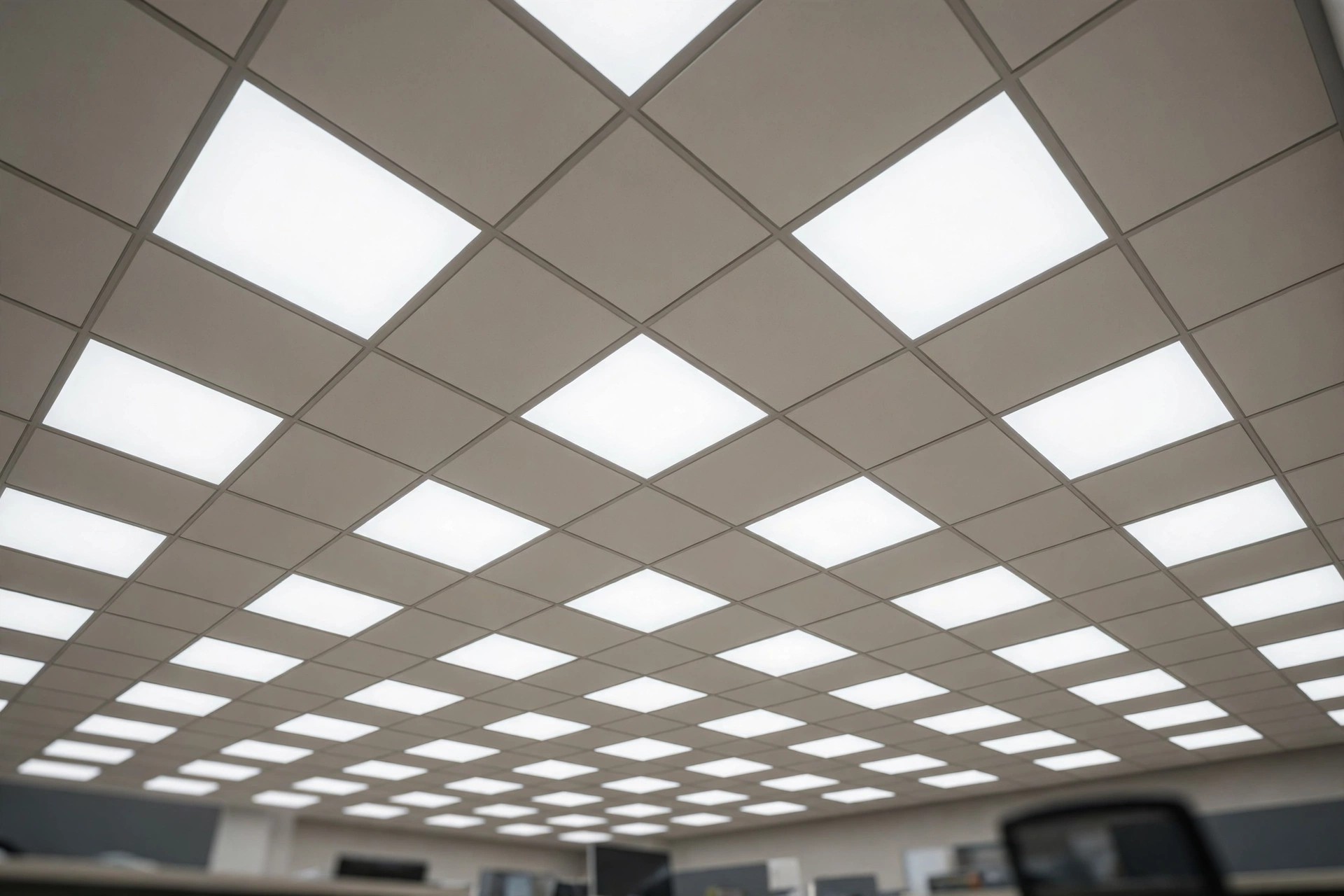 Grid ceiling with an even layout of square LED panels giving uniform light over office desks