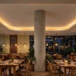 Warm cove-lit false ceiling over a restaurant dining area with pendant lights above tables
